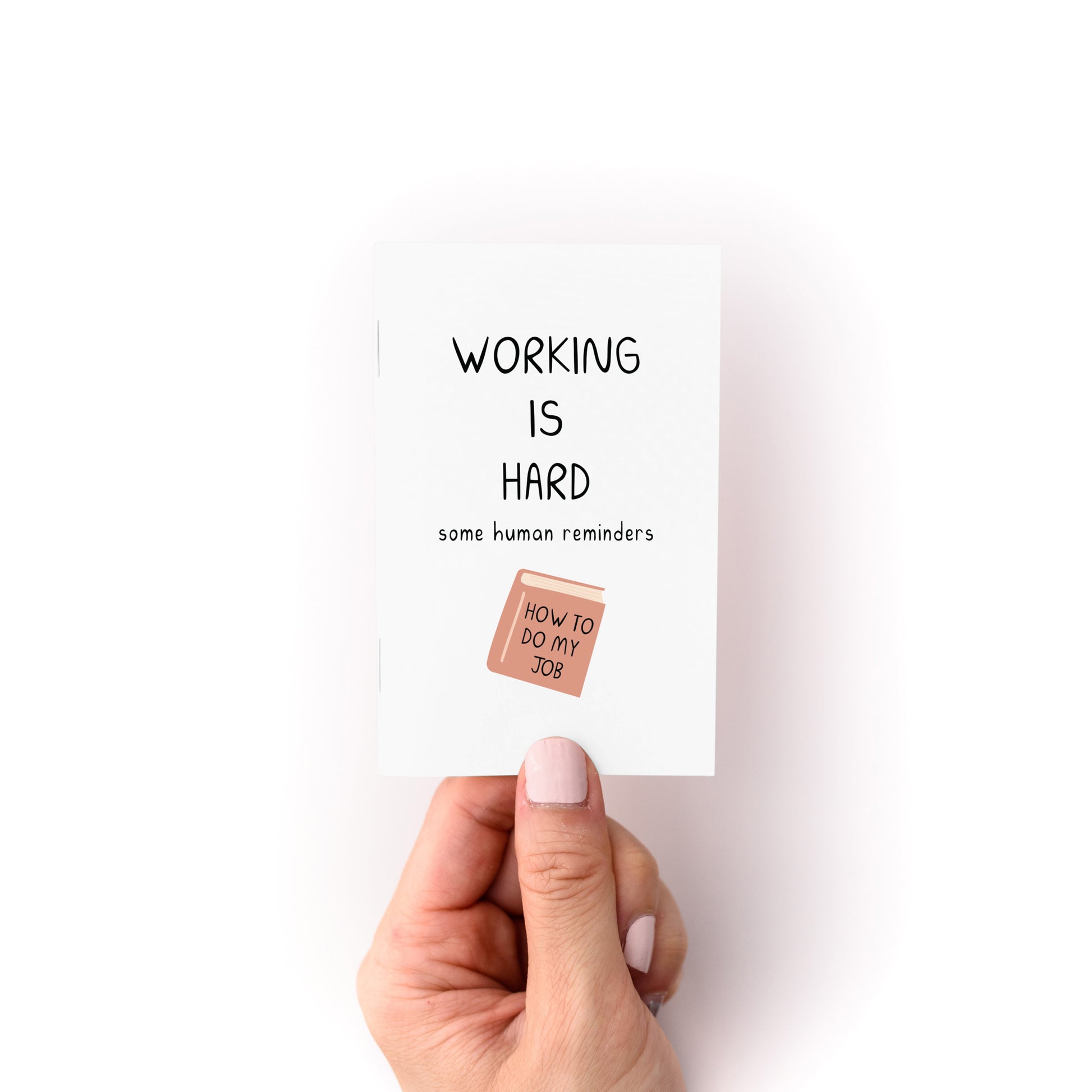 Hand holding the Working is Hard Zine with reminders and a small illustration of a book titled How to Do My Job.