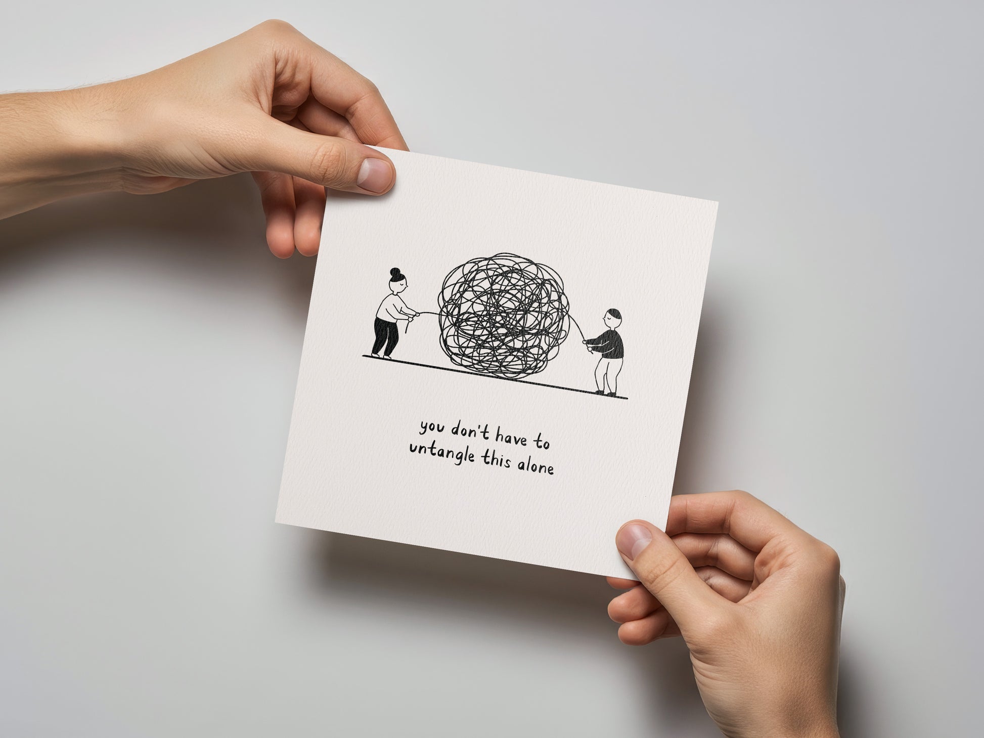 Square sympathy card held by two hands showing two figures untangling a large ball with text below.