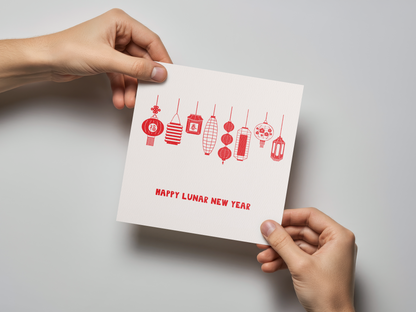 Square greeting card held by two hands, featuring a row of eight distinct red paper lanterns hanging above the text "Happy Lunar New Year" on a white textured background.