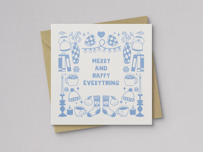 Square greeting card featuring light blue illustrations of winter-themed items including mittens, hats, socks, candles, mugs, vases, and books arranged around the text "Merry and Happy Everything," paired with a kraft paper envelope.