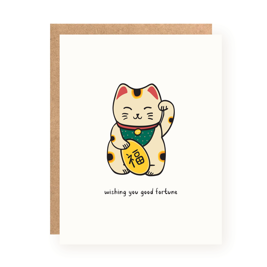 White greeting card featuring a cute hand-drawn lucky cat wearing a green bib and holding a gold coin with Chinese characters, accompanied by the message "wishing you good fortune" and a brown kraft envelope behind.