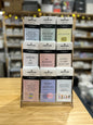 Wooden display rack holding 54 colorful Kwnotations zines with thoughtful titles arranged in three rows on wooden table