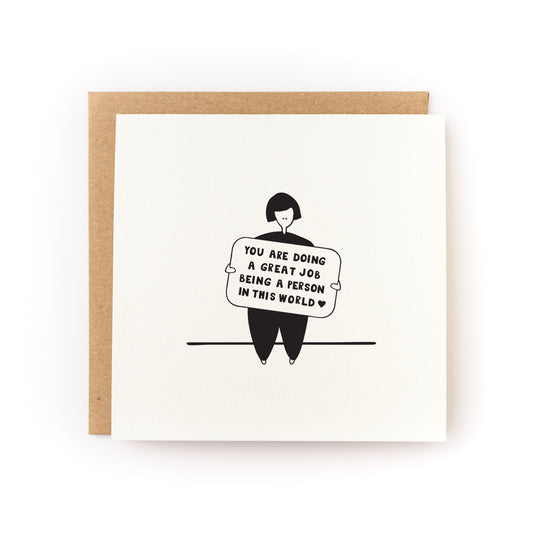 Square white greeting card featuring a simple black line illustration of a person holding a sign with the handwritten message "You are doing a great job being a person in this world," paired with a brown kraft envelope.