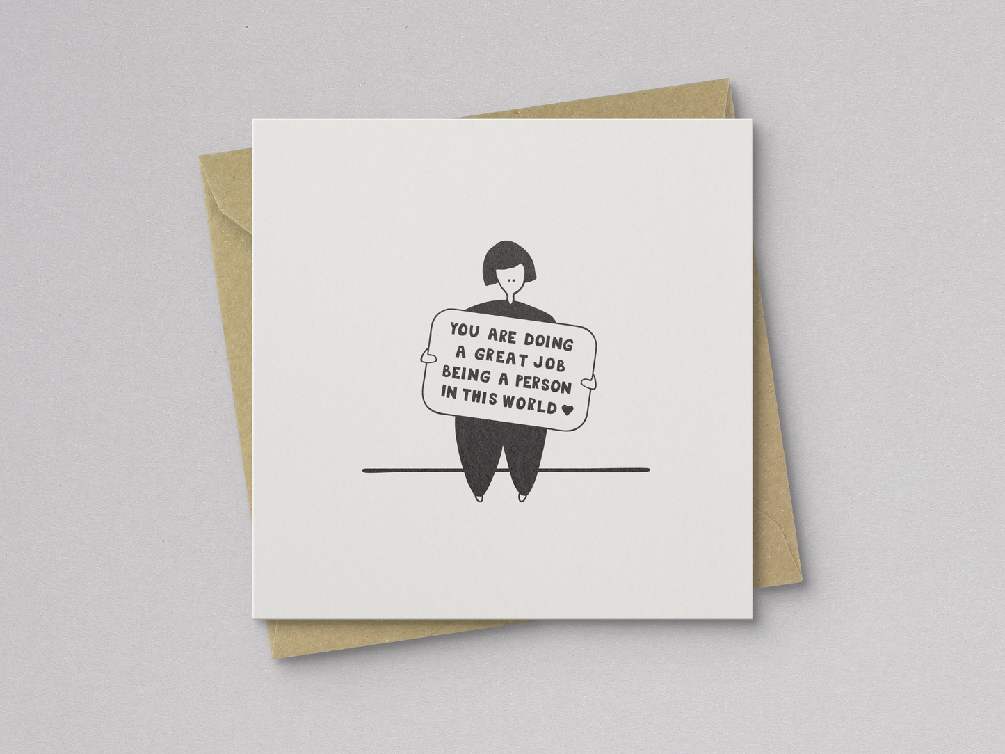 Square white greeting card featuring a simple black line drawing of a person sitting and holding a sign with the handwritten message "You are doing a great job being a person in this world," paired with a brown kraft envelope.