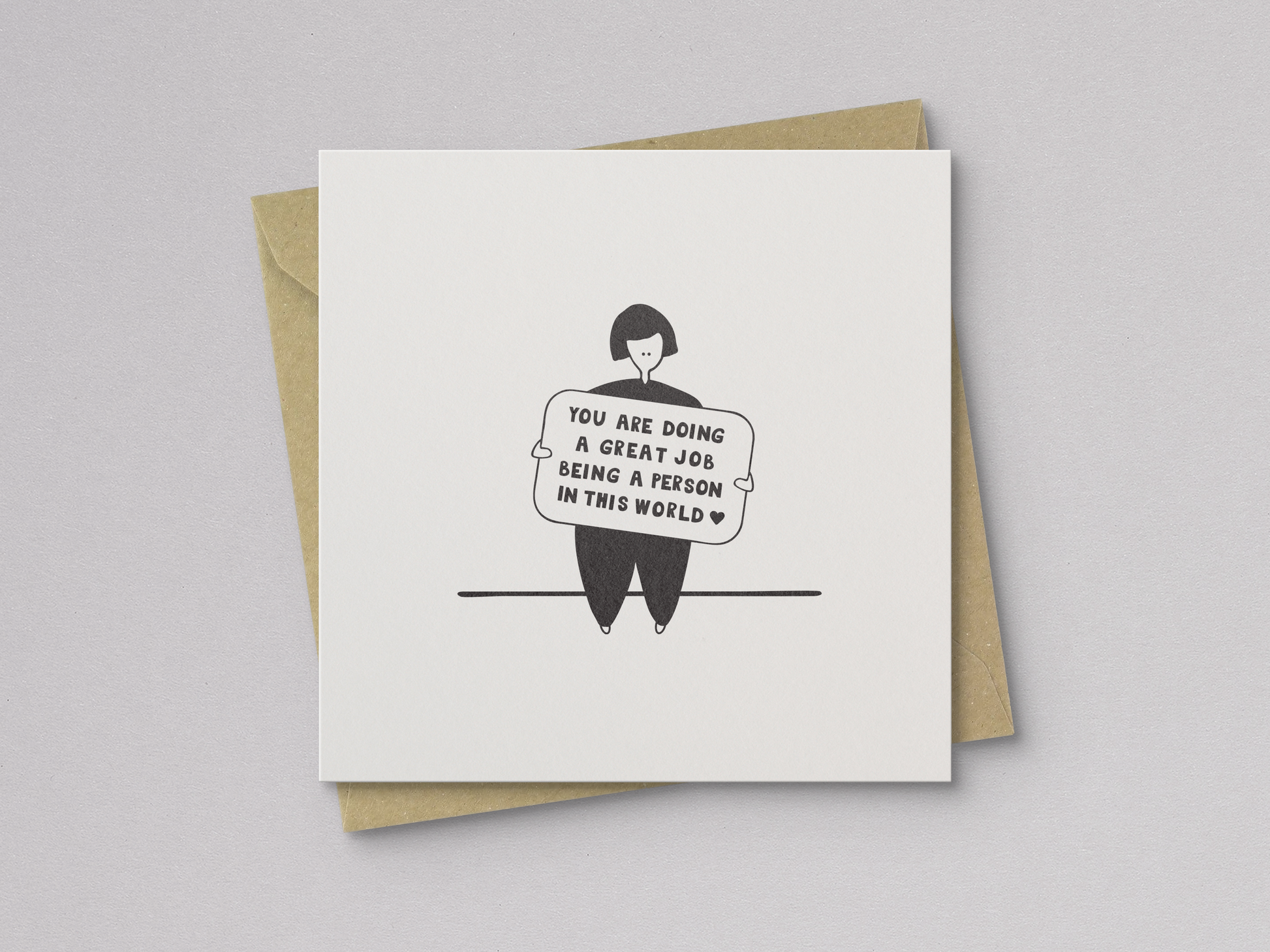 Square white greeting card featuring a simple black line drawing of a person sitting and holding a sign with the handwritten message "You are doing a great job being a person in this world," paired with a brown kraft envelope.