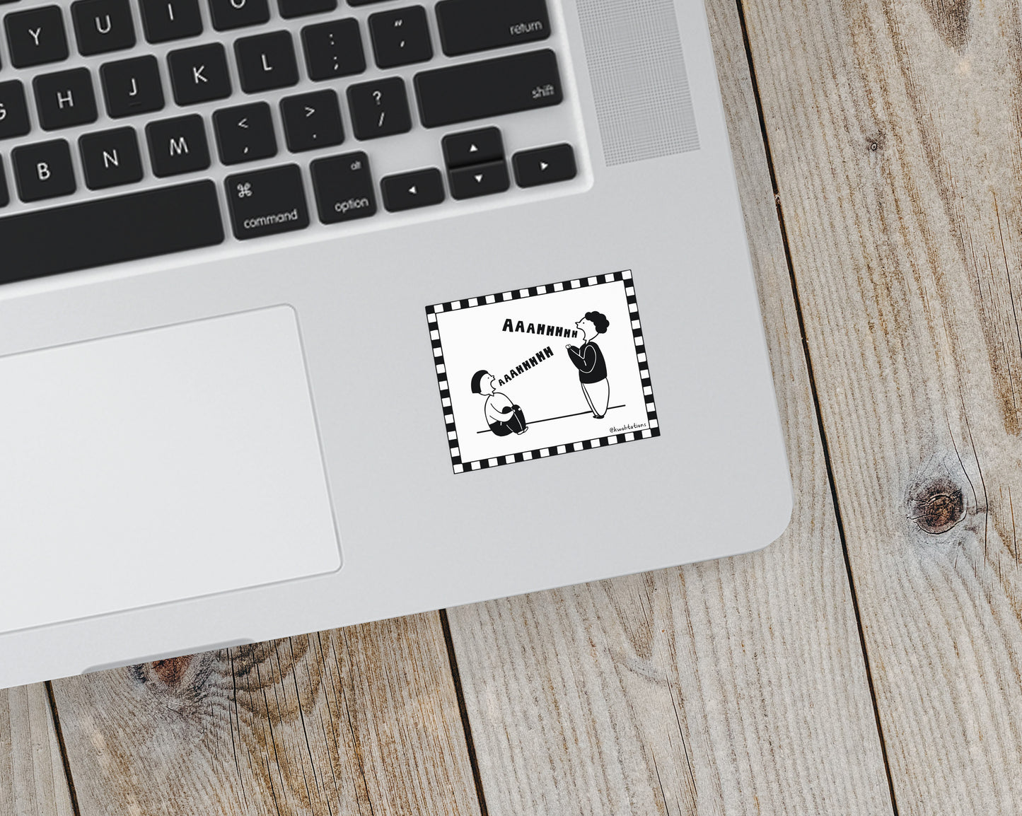 Black and white sticker on a laptop showing two stylized figures shouting "Aaaahhhh" inside a checkered border with one person standing and the other sitting on the ground.
