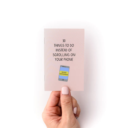 Hand holding the "30 Things to Do Instead of Looking at Your Phone Zine" with a phone illustration on the cover.