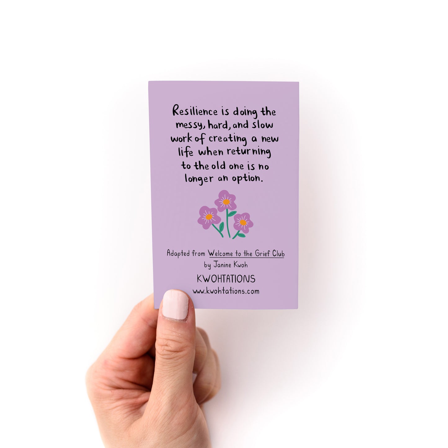 Hand holding a lilac card with handwritten resilience quote and three purple flowers on a white background.